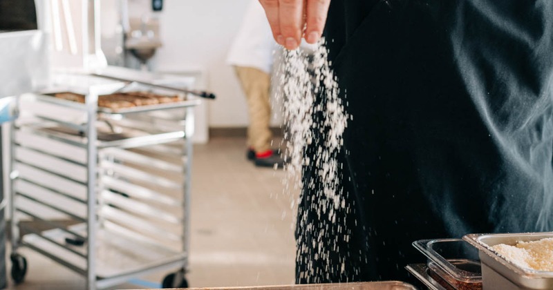 Chef sprinkling grated cheese over a freshly baked pizza