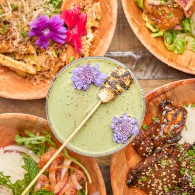 Kyoto Fog cocktail garnished with flowers and a marshmallow, surrounded by plates of food.