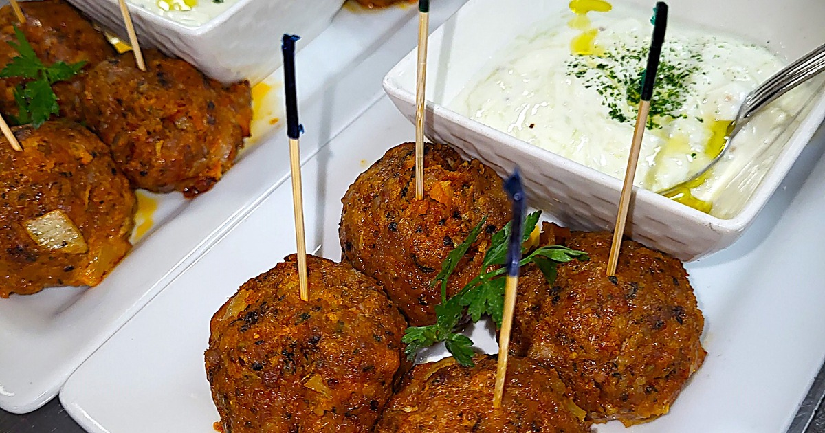 Golden-brown meatballs on a white plate, accompanied by tzatziki sauce