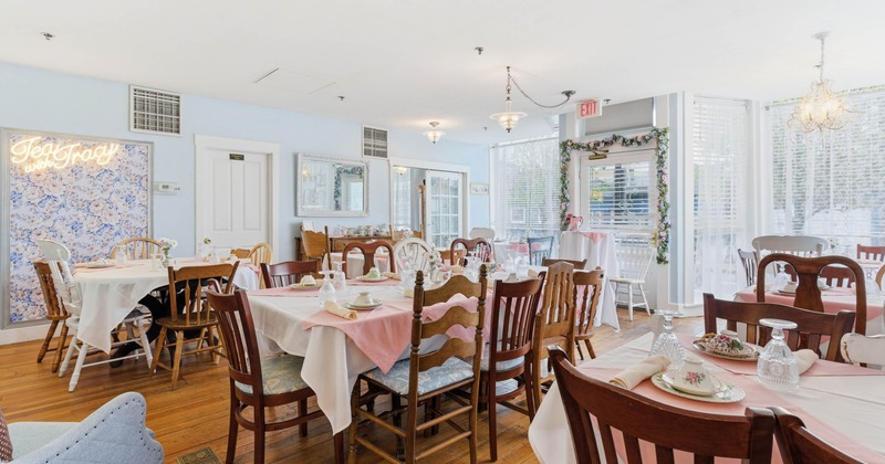 A cozy tea room with tables set in fine china, pink table runners, and wooden chairs