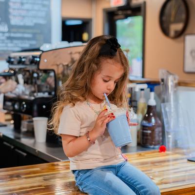 A child sitting on the counter and drinking a blue drink topped with whipped cream.
