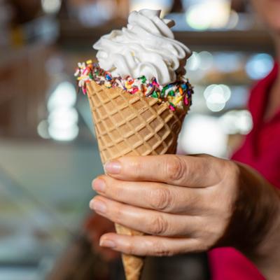 Person holding a soft-serve ice cream cone with rainbow sprinkles.