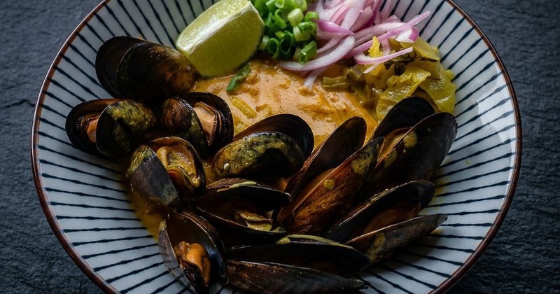 Khao soi mussels with noodles served alongside fresh garnishes