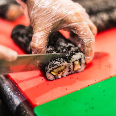 Chef cutting a sushi roll on the board.