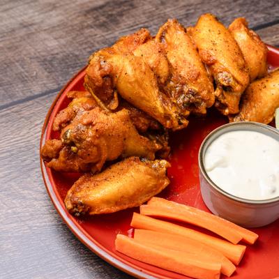 Crispy buffalo wings served with carrot sticks and creamy dipping sauce on a red plate.