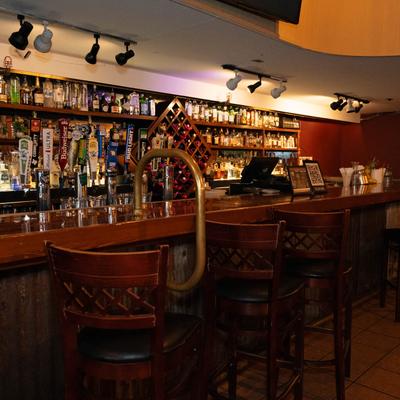 Bar interior with high wooden stools, a polished counter, and a variety of liquor bottles.