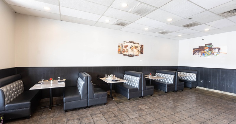 Restaurant interior with black and silver tufted booths, set tables, and abstract art on walls