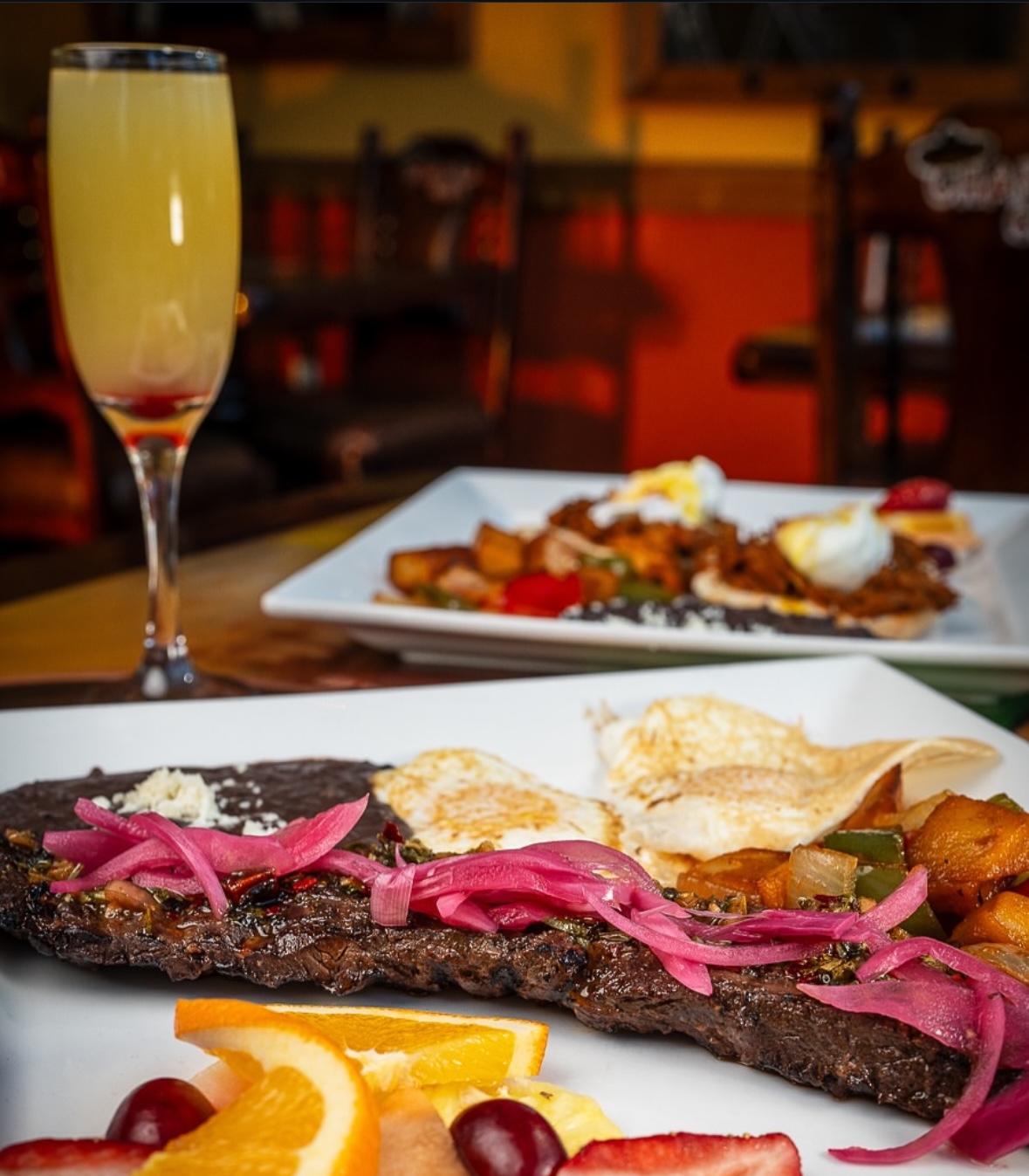Grilled steak with pickled onions, fried eggs, potatoes, and a mimosa