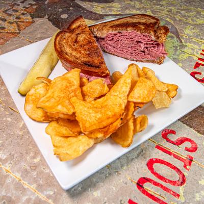 Reuben Sandwich sliced in half and served with chips and a pickle.