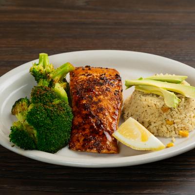 Norwegen salmon served with rice, broccoli, avocado slices and a lemon wedge.