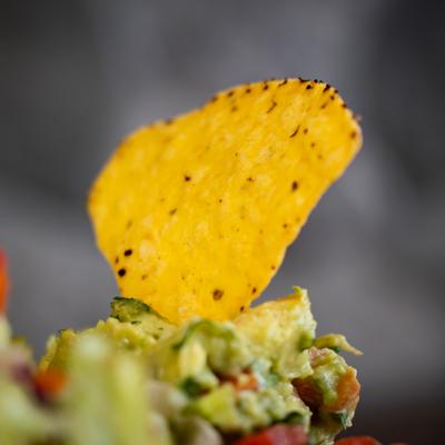 Tortilla chip dipped in chunky guacamole with avocado and tomato.