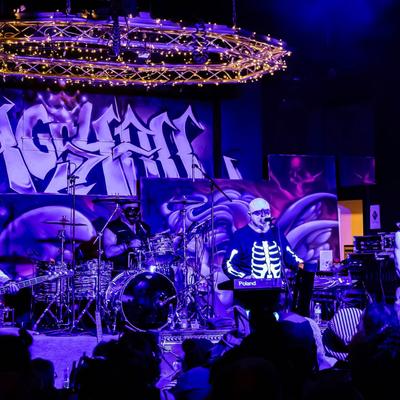 A musician in a skeleton shirt performing on stage with a band.