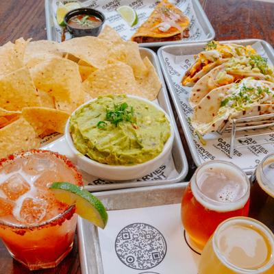 Tacos, chips with guacamole, and drinks on a restaurant table.