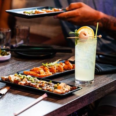 A wooden table holds plates of appetizers and an iced lychee cocktail.