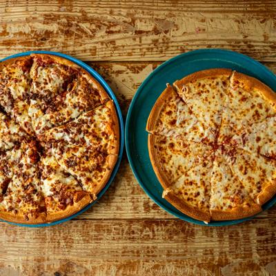 Meat pizza and cheese pizza on a wooden table.
