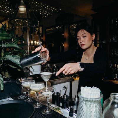 Bartender pouring a cocktail into glasses using a strainer.