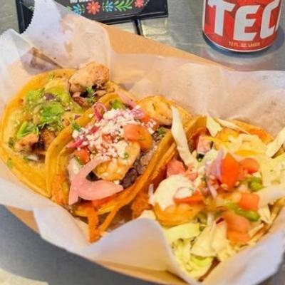 colorful plate of 3 tacos with guacamole and pico de gallo, a tecate beer in the background.