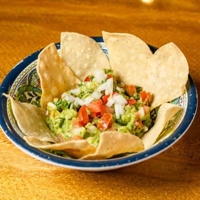 Guacamole garnished with tomatoes, onions, and cilantro, served with tortilla chips.