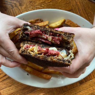Reuben sandwich held over a plate with fries.