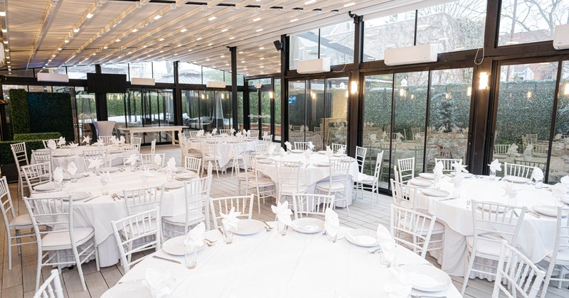 An indoor event space with white table settings and glass walls overlooking a garden