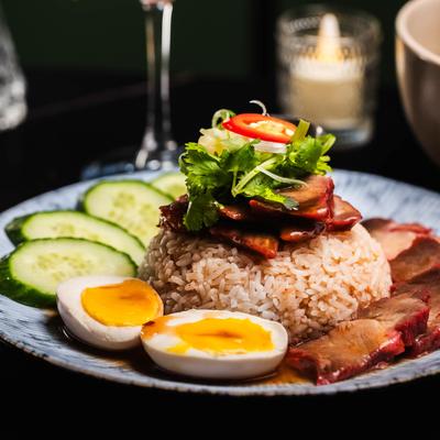 Marinated pork belly with rice, egg, cucumbers, and herbs, served with a cocktail.