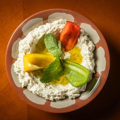 A bowl of creamy dip garnished with red, green, and yellow pepper slices, and mint leaves.