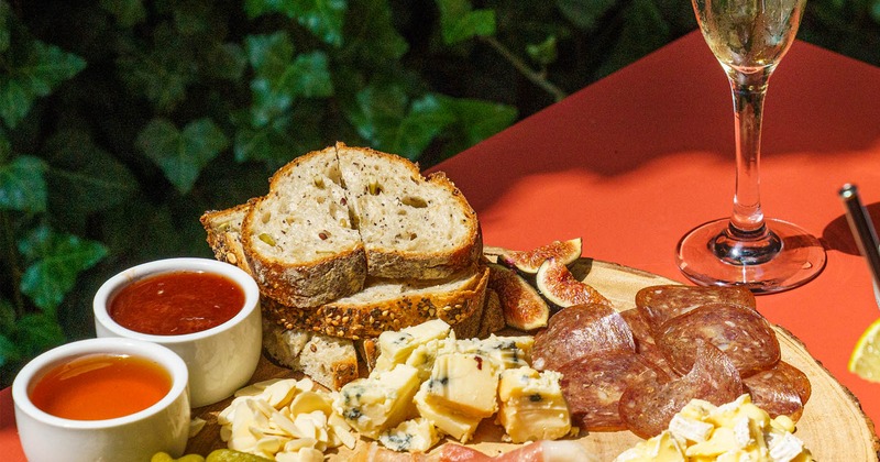 Charcuterie board with a flute glass of sparkling wine, set on a red table outdoors
