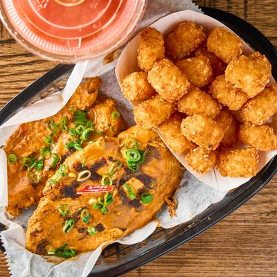 Grilled chicken breast served with tater tots, top down view.