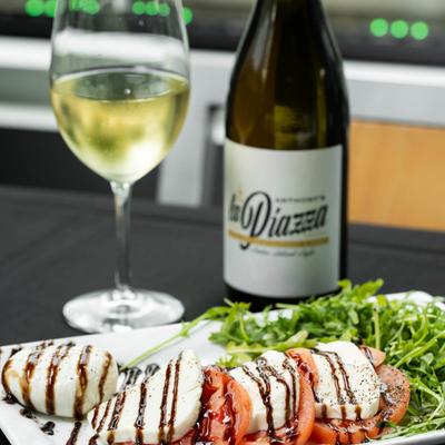 Burrata Caprese plate accompanied with a bottle and glass of white wine.