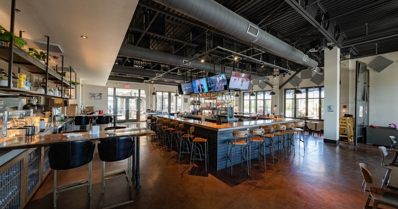 Interior, bar in the center, hanging TV sets, bar stools and tables, entrance in the back