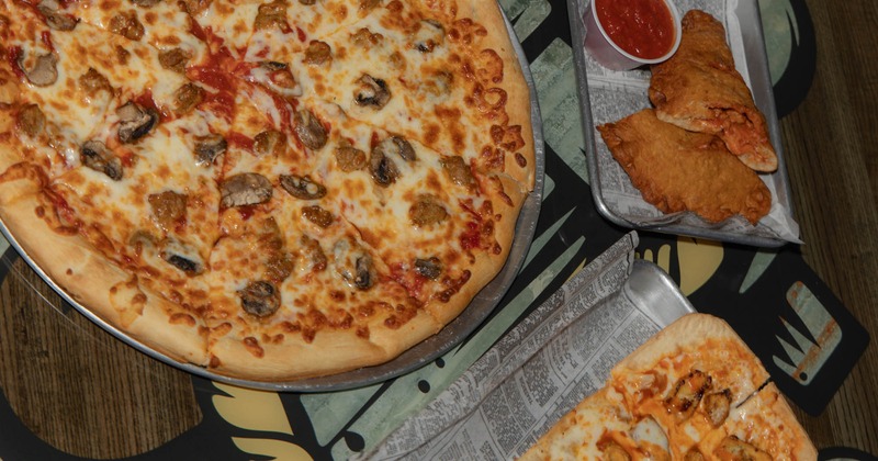 Close up of a table with pizza, alongside calzones with marinara sauce and a rectangular flatbread