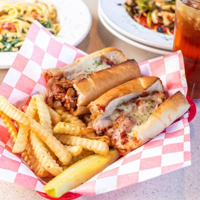 Halved chicken sub sandwich with melted cheese and crinkle-cut fries on checkered paper.