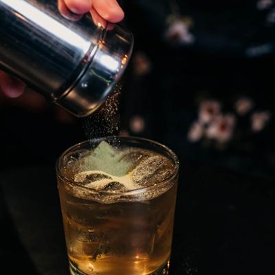 Whiskey Business cocktail being garnished with matcha dust.