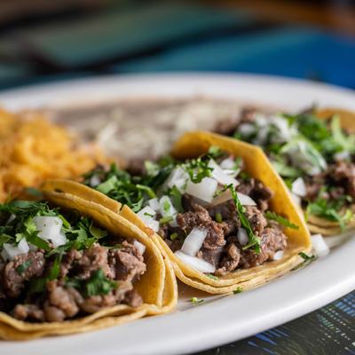 Steak tacos, with onion and cilantro, with Mexican rice and refried beans on the side