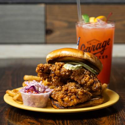 Nashville Hot Sandwich served with coleslaw and fries, alongside a cocktail.
