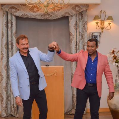 The owners in colorful blazers engaging in a celebratory handshake.