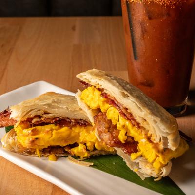 Breakfast sandwich with egg, cheese and bacon, served on banana leaf.