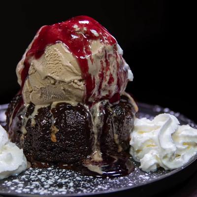 Chocolate lava cake topped with ice cream, berry sauce, and whipped cream.