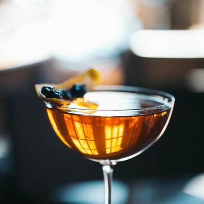 Close-up of an amber-colored cocktail in a coupe glass garnished with a dark berry and citrus peel.