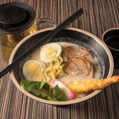 Tonkotsu ramen served on a table with tea pot and cup of tea.