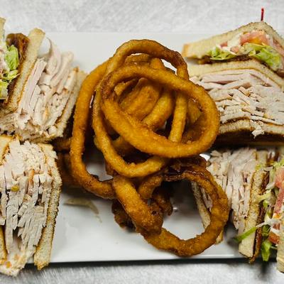 Triple-decker turkey club sandwich served with a side of onion rings.