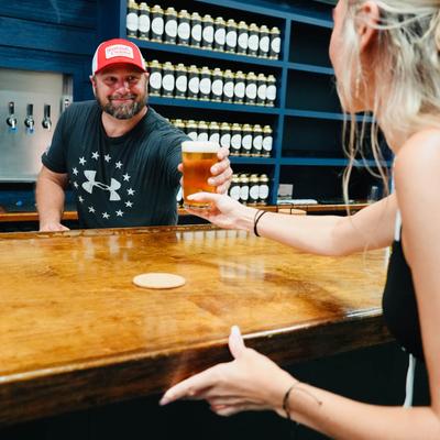 A staffer serves a glass of craft beer to a customer at the bar counter.