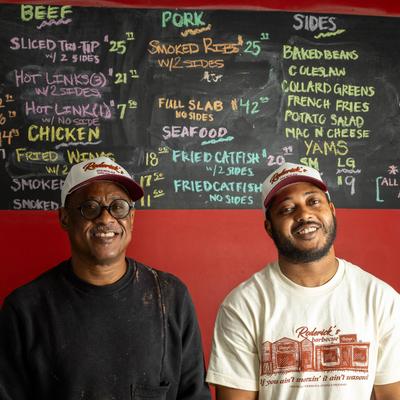 Chef and Owner posing together for a shot in front of a wall menu, head shot.