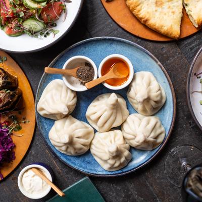 Georgian soup dumplings with black pepper and clarified butter on round plate amidst other dishes on dark table