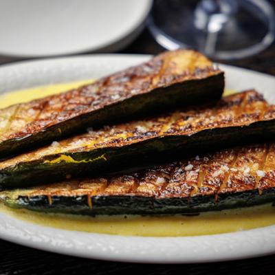 Grilled zucchini halves with charred crosshatch marks and salt with yellow sauce..