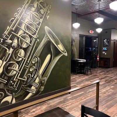 Interior featuring a mural of a saxophone, wooden floors, and pendant lights.
