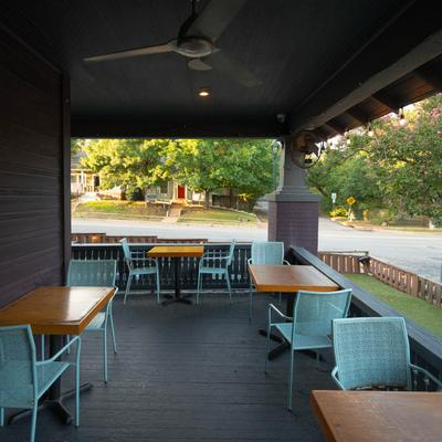 Outdoor patio with wooden tables and blue chairs overlooking a street and trees.