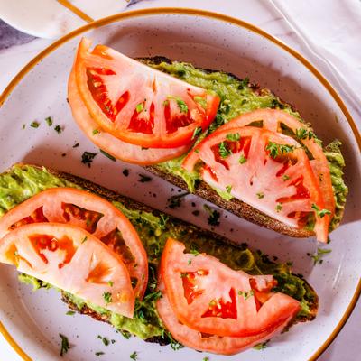 Avocado toast topped with tomato slices and fresh herbs.
