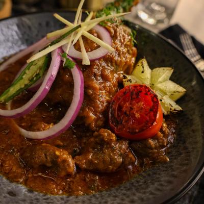Chicken Masala garnished with sliced red onions, a green chili, and a tomato half.