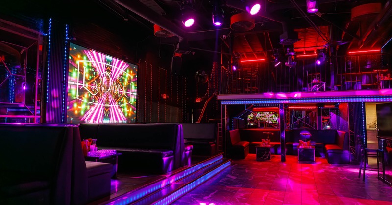 Vibrant interior - colorful LED lighting, leather seating booths, a large screen and neon accents.